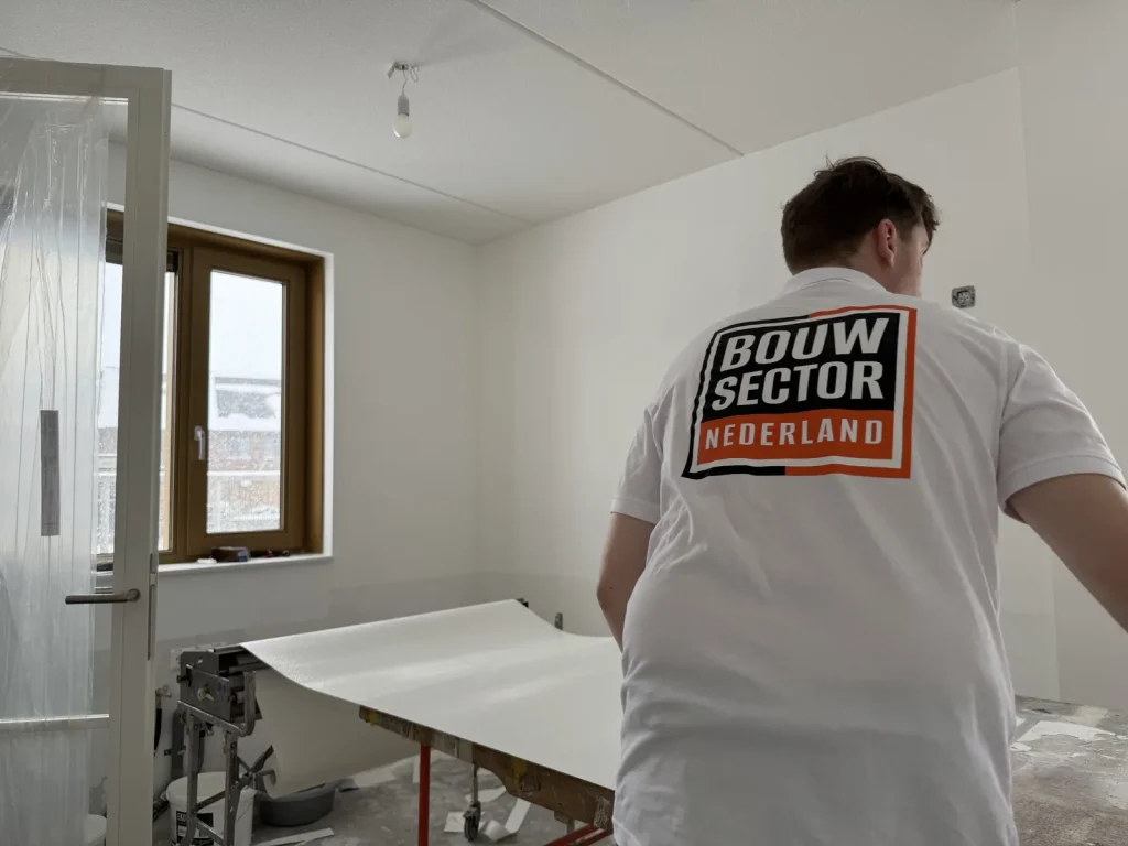 Behanger legt een baan vlies klaar op de plaktafel in een kale slaapkamer