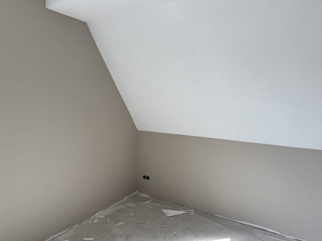 Zolderkamer met schuine wand, beige gesausde muren en een wit dakvlak