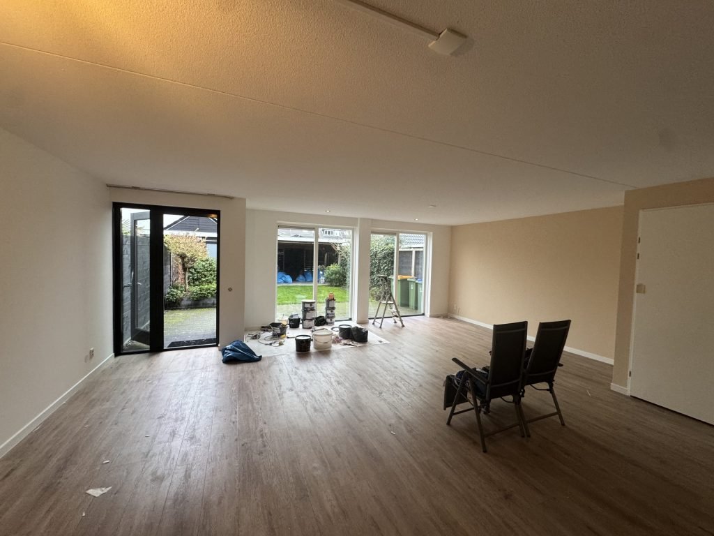 Ruime woonkamer met lichte gesausde wanden, houten vloer en tuindeuren