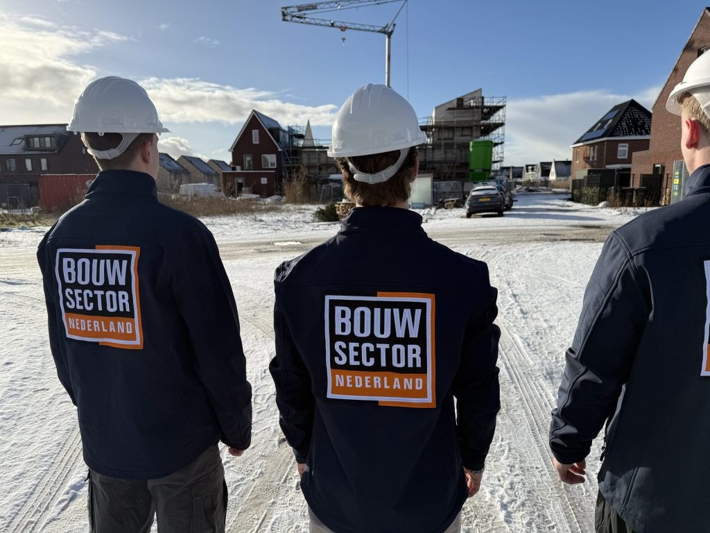 Drie vakmensen in bedrijfsjas kijken samen naar een woning in aanbouw